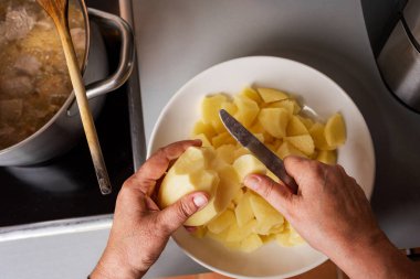 Kadının elleri güveçte ete ilave etmek için mutfakta patatesleri parçalara ayırıyor. Yakın plan..