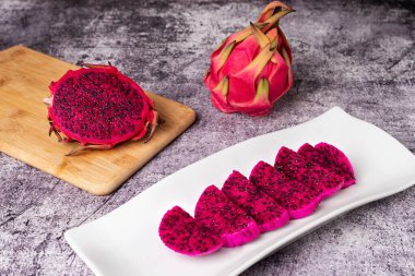 Pitaya ya da ejderha meyvesi, yarım pitahaya pembeyi siyah tohumlar ve yemeye hazır bir tabak meyveyle ortaya çıkarıyor..