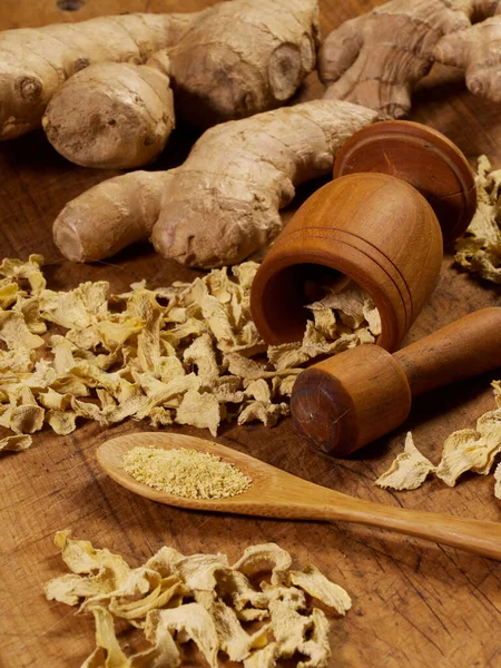 Kurumuş ve taze zencefil, tahta bir kesme tahtasının üzerinde havan ve tokmakla.