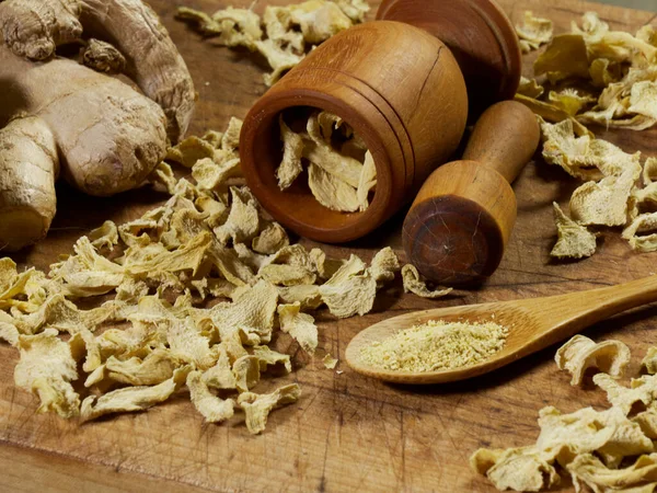 Kurumuş ve taze zencefil, tahta bir kesme tahtasının üzerinde havan ve tokmakla.