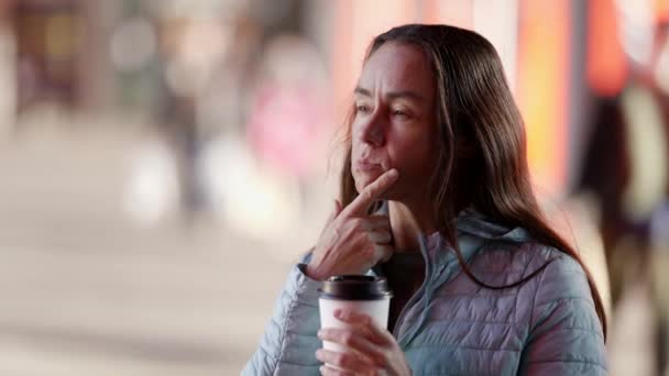 Close-up portret van een attente vrouw van middelbare leeftijd op straat met koffie in haar hand aanraken van haar kin — Stockvideo