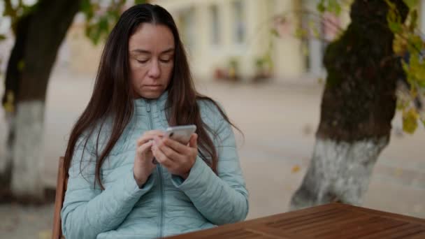 Πορτρέτο μιας ενήλικης γυναίκας που κρατά ένα κινητό τηλέφωνο στα χέρια της σε εξωτερικούς χώρους. Ένα κοντινό πλάνο μιας απογοητευμένης γυναίκας κοιτάζει την οθόνη smartphone σε ένα δρόμο της πόλης — Αρχείο Βίντεο