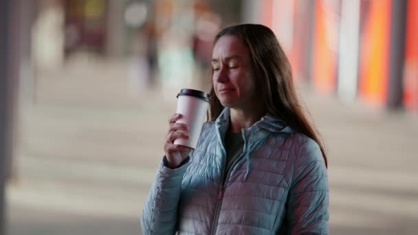 Взрослая задумчивая женщина пьет кофе на улице из бумажного стаканчика смотрит в сторону — стоковое видео