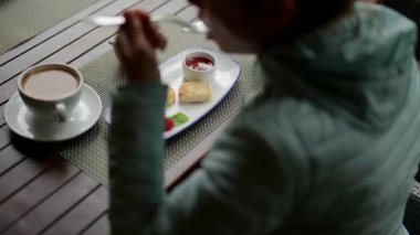 Peynirli kekin üzerine ekşi krema serpiştirmek için bir kadının elini yakın plan çekeceğiz. Lokantada sıcak bir içecek ve tatlı getiren bir kadın kahvaltı yapıyor.