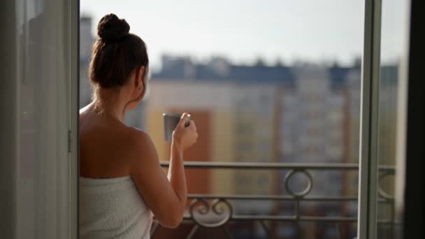 Una mujer adulta que admira sale del apartamento, se encuentra en el balcón de la terraza, admirando la pintoresca vista del amanecer. El concepto de una mañana tranquila. — Vídeos de Stock