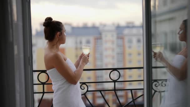En voksen kvinde i hvid frakke går ud på balkonen om morgenen for at drikke et glas champagne. Kvindelig alkoholisme – Stock-video