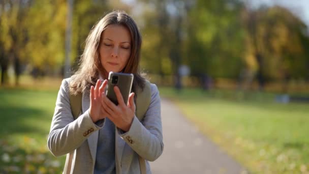 Seorang wanita dewasa menginstal seorang navigator pada perangkat telepon modern, berjalan melalui jalan-jalan di taman kota. si penjelajah berjalan-jalan dan menerbitkan pos baru di situs web — Stok Video