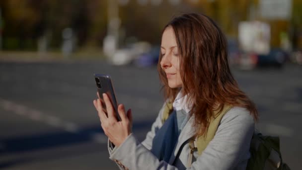 Πορτρέτο μιας γλυκιάς, ευχάριστης ενήλικης γυναίκας που μένει ενημερωμένη με εκδηλώσεις σε μια υπαίθρια κοινωνική εφαρμογή χρησιμοποιώντας ένα smartphone online στο συνδεδεμένο Internet — Αρχείο Βίντεο