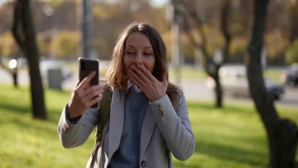 Dorosła kobieta w eleganckich ubraniach, stojąca na ulicy i używająca smartfona do komunikacji wideo w Internecie. emocjonalnie rozmawiać z przyjaciółmi podczas podróży — Wideo stockowe