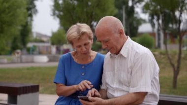 Ellerinde akıllı bir telefon tutan mutlu yaşlı bir çift cep telefonu ekranına bakar ve komik fotoğraflara bakar. Ailenin büyük anne ve büyük babası eğleniyor.
