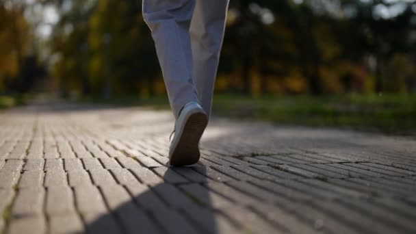 Primer plano de las zapatillas modernas caminando sobre baldosas de piedra, pasos en zapatos con sombra en un día soleado en cámara lenta — Vídeo de stock