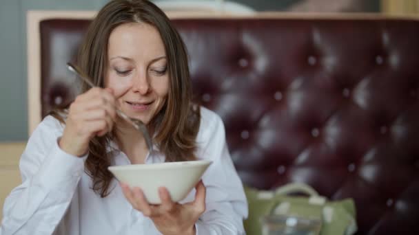 Retrato de uma bela mulher adulta segurando um prato de salada de legumes e comendo em um café elegante, olhando para a câmera. Uma mulher está almoçando em um restaurante — Vídeo de Stock