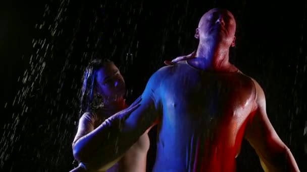 Un hombre deportivo reza en la noche bajo la lluvia, su mujer está a su lado y toca su cuerpo — Vídeos de Stock