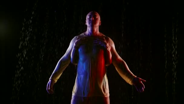 Um homem muscular fica na chuva à noite mãos femininas gentis tocando o corpo atlético — Vídeo de Stock