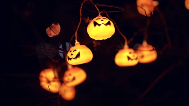 Primo piano di una ghirlanda jack lanterna zucche bagliore al buio su un albero della città — Video Stock