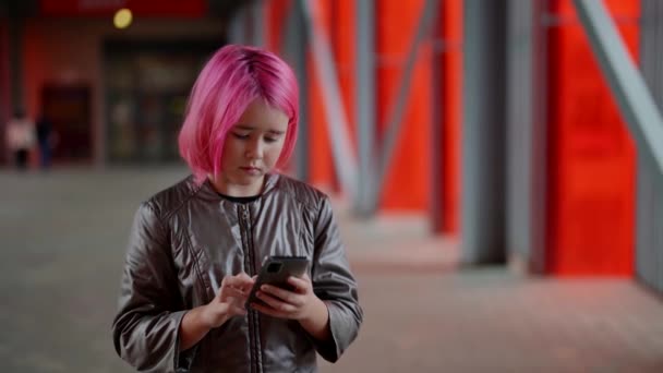 Adolescente com cabelo rosa olha para um telefone celular jogando em redes sociais — Vídeo de Stock