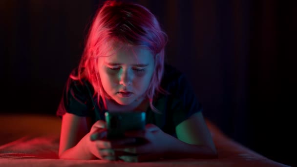 Een slapeloze tienermeisje ligt 's nachts in bed en speelt met haar telefoon — Stockvideo