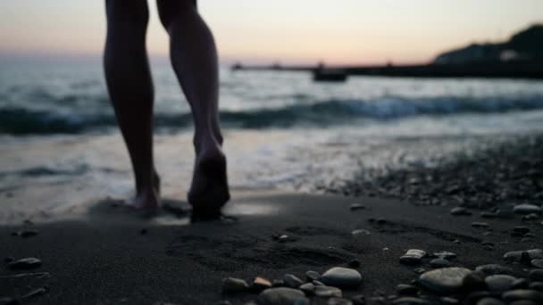 Mujeres pies caminando descalzas tarde en la noche en una playa de arena en el mar. Una ola lava los pies de las mujeres. — Vídeo de stock