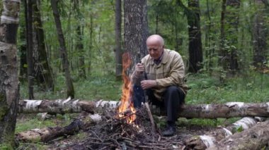 Yaşlı, yalnız bir turist ormanda kamp ateşiyle ısınıyor. Sonbahar yürüyüşünde çok üşümüştü..