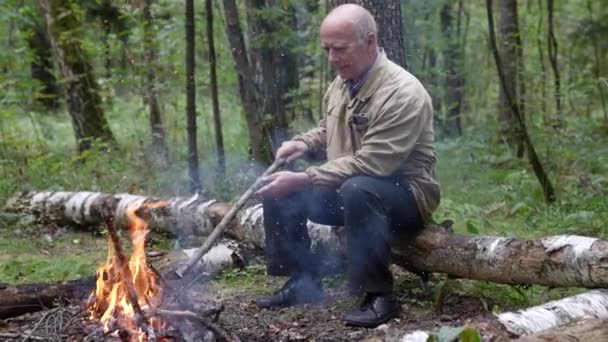 O viajante está sentado ao lado da fogueira. Um turista está descansando perto da fogueira no acampamento, à noite ele monta acampamento na floresta. Um turista masculino está de férias na natureza — Vídeo de Stock