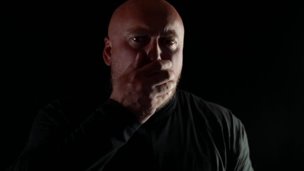 En skallig man med ont i halsen hostar våldsamt på svart bakgrund — Stockvideo