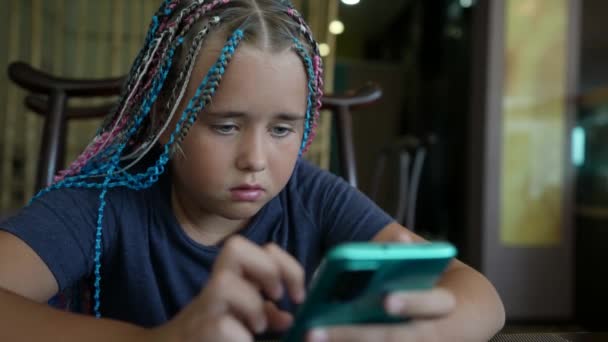 O adolescentă frumoasă cu afro-pigtail-uri, așezată într-o cafenea, relaxantă, mesaje text prietenilor, navigarea pe rețelele sociale, navigarea pe Internet, uitându-se la cameră — Videoclip de stoc