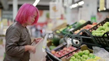 Süpermarkette pembe saçlı bir genç meyve ve sebze reyonunda elma seçiyor.