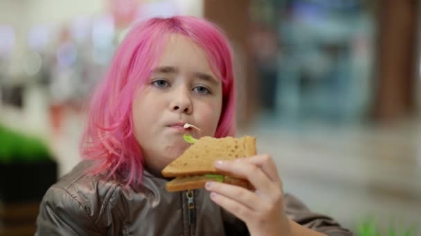 Triste adolescent sans abri aux cheveux roses mange un sandwich dans un café — Video