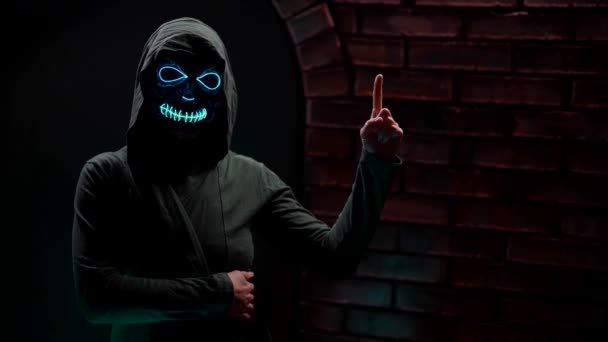 Halloween night party sinister death in a hoodie against a brick wall with a finger gesture shows up — Stock Video