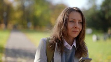 Neşeli yetişkin bir turist modern bir telefon cihazına seyir subayı yerleştiriyor, şehir parkı koşullarında sokaklarda yürüyor.