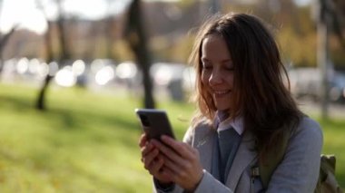 Yetişkin bir Avrupalı kadın elinde telefonuyla şehir parkında video bağlantısıyla dolaşıyor.