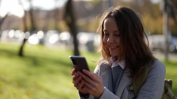 Una mujer europea bastante adulta caminando a través de un parque de la ciudad con un teléfono en sus manos gesto por enlace de vídeo — Vídeos de Stock