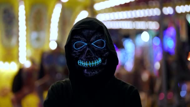 Портрет жінки в масці смерті, що світиться неоновим вогнем на тлі парку розваг — стокове відео