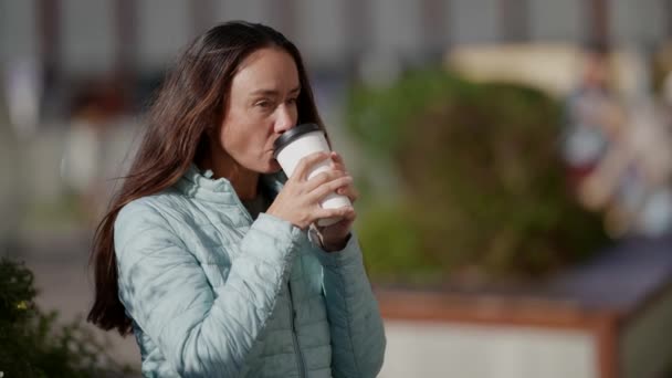 Atrakcyjna dorosła beztroska kobieta pije kawę na wynos z papierowego kubka na ulicy — Wideo stockowe