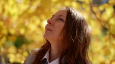 Güneşli bir günde, sonbaharda parkta yürüyen çekici bir kadının yakın plan portresi. Sonbaharda açık havada mutlu ve güzel bir kadının yüzü..