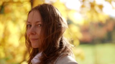 Güneşli bir sonbahar gününde parkta yürüyen mutlu yetişkin bir kadının yakın plan portresi. Hoş görünümlü yetişkin bir kadın yürürken olumlu duygular hisseder..