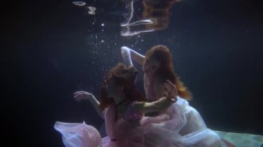 Havuzun karanlık derinliklerinde yüzen, su sıçratan ve elbiselerle oynayan romantik bir kadın eşcinsel çift.