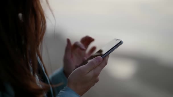 Сторона просмотра руки девушки с помощью смартфона на улице в вечернее время, печатая сообщение. Крупный план рук молодой женщины — стоковое видео