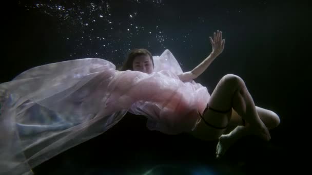 Encantadora joven posando bajo el agua en la piscina. Una mujer vestida de blanco en una sesión de arte. Escena surrealista con una chica artística. — Vídeos de Stock