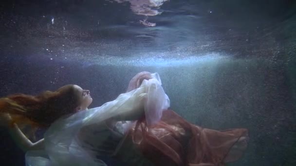 Una mujer joven y bonita, nadando en el fondo de la piscina en un hermoso vestido, una dama participa en una actuación artística — Vídeos de Stock