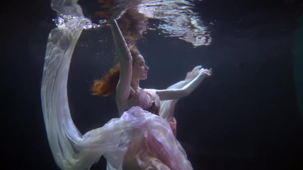 En ung och smal kvinna, simmar under vattnet i en vacker klänning, en dam deltar i en konstnärlig föreställning — Stockvideo