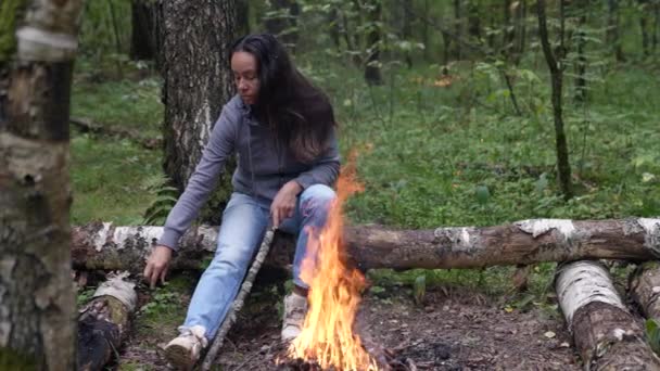 妇女坐在林地篝火边，焚烧干枯的树枝，徒步旅行 — 图库视频影像