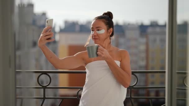 Жінка середнього віку з неприємними плямами і кавою приймає селфі на балконі в ранковий час — стокове відео