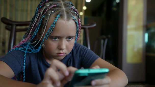 Primer plano de una cara de adolescente con un teléfono inteligente, en casa. Un niño pasa tiempo en una red social usando un teléfono móvil. Una chica usando un teléfono móvil para juegos. — Vídeo de stock