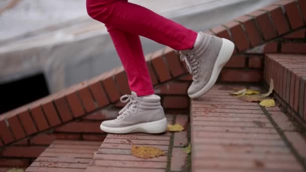 Höst gata stil, närbild av kvinnliga ben i röda byxor och vita sneakers, promenader ner för trappor — Stockvideo