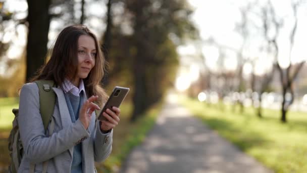 Ενήλικη γυναίκα περιμένει κάποιον στο πάρκο, καλώντας από το κινητό τηλέφωνο, κινηματογραφικό πορτρέτο της κυρίας στο πάρκο — Αρχείο Βίντεο