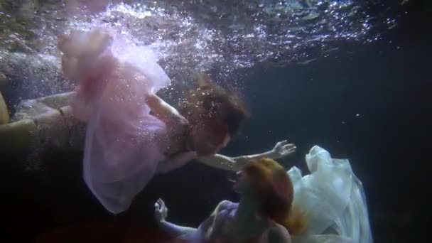 Két kecses nő, úsznak a víz alatt egy gyönyörű ruhában, egy hölgy részt vesz egy művészi előadáson. — Stock videók