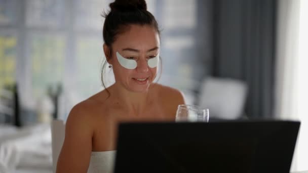 Брюнетка женщина с косметическими пластырями под глазом общается по видеосвязи в ноутбуке — стоковое видео