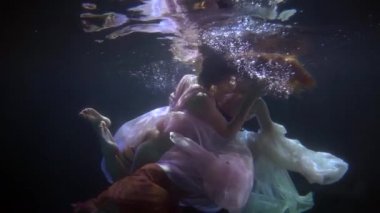 Peri masalındaki denizkızları gibi su altında elbiseli iki büyüleyici kadın havuzda yüzüyor.