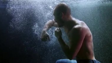 Erkek sporcu su altında boksör, yumrukları eğitiyor ve karanlık bir havuzun altında dalıyor.
